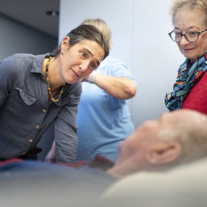 Palliaviva-Mitarbeiterin Livia de Toffol (links) beugt sich zu einem Patienten, der im Bett liegt. Daneben steht seine Frau. Foto: Gaëtan Bally